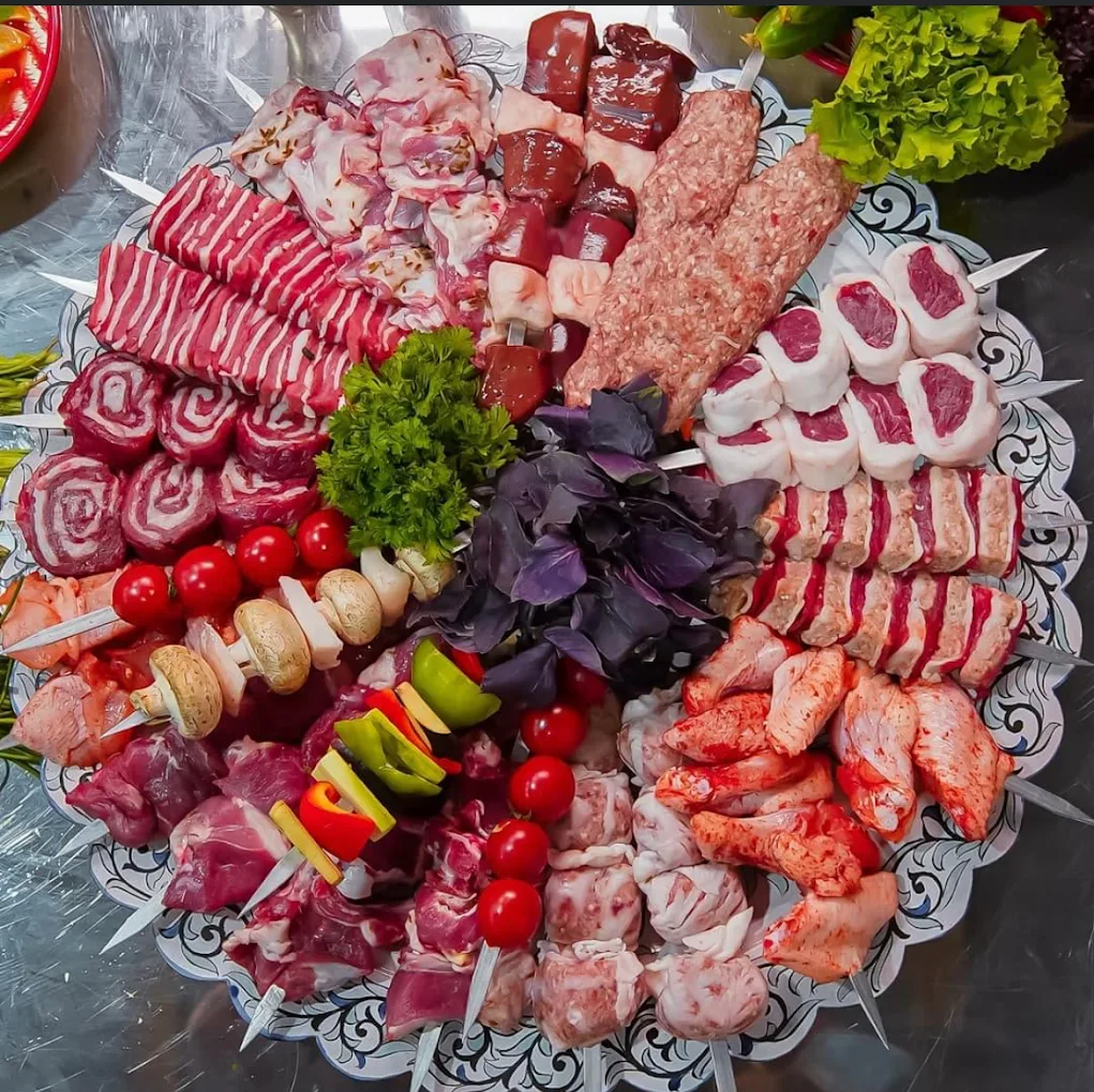 A large patterned platter at Shashlik House NYC holding skewers of lamb, beef, chicken, liver and lula kebab, threaded and waiting to be grilled