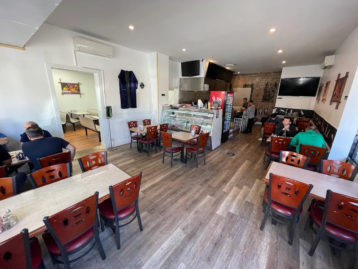 The dining room at Shashlik House NYC, with wooden tables, red-cushioned chairs and a refrigerated skewer case beside the counter