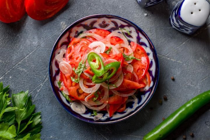 Achichuk salad of sliced tomato, onion and green chilli in a patterned bowl