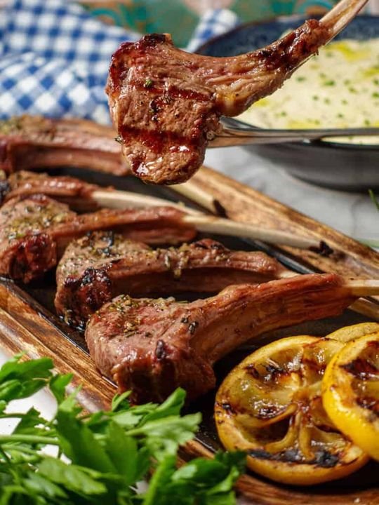 Three grilled baby lamb chops on a wooden board with charred lemon