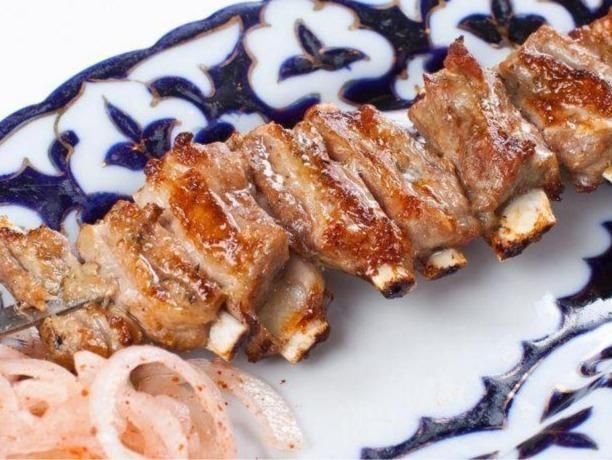 Charcoal-grilled lamb ribs on a skewer with sliced onion